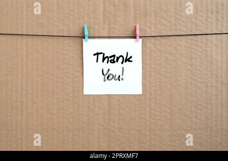 Thank you! Note is written on a white sticker that hangs with a clothespin on a rope on a background of brown cardboard Stock Photo