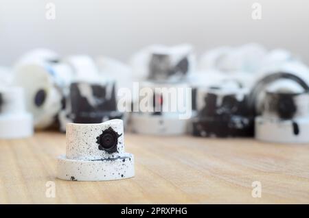 Several plastic nozzles from a paint sprayer that lie on a wooden surface against a gray wall background. The caps are smeared in black paint. The con Stock Photo