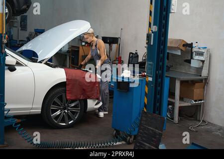 Young craftswoman inspects a car engine under the hood Stock Photo