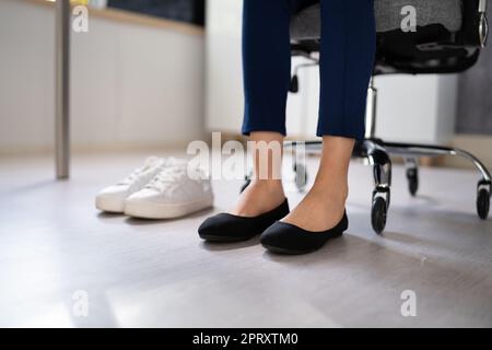 Pair Of A White Sport Shoes Besides Businesswoman's Legs In Office Stock Photo