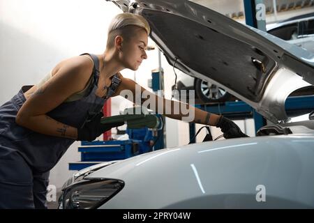 Car mechanic works under hood of car with special scanner Stock Photo