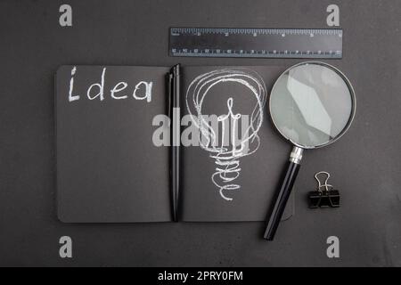 top view idea written on black notebook binder clip lupa ruler pen on dark background Stock Photo