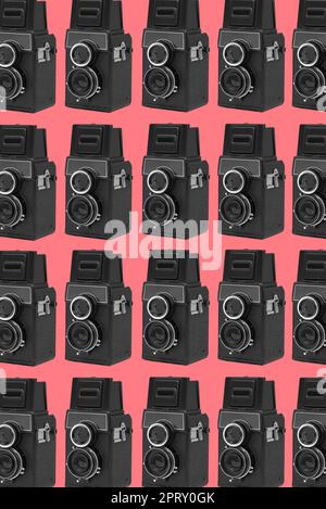 some black retro medium format film cameras arranged in different lines forming a mosaic pink background Stock Photo
