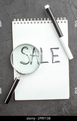 top view sale written on spiral notebook lupa black marker on black background Stock Photo