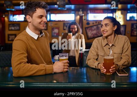 Young couple flirting and drinking beer sitting at sport bar counter. Handsome stranger, nice conversation of young people in pub Stock Photo