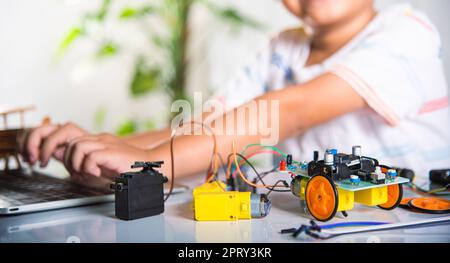 Asian kid boy learns coding and programming with laptop for Arduino robot car, Little child students typing code in computer online with car toy, STEA Stock Photo