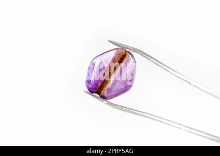 Bright transparent violet amethyst crystal gem in the pincers on light background with copy space close up. Stock Photo