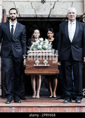 Funeral, church and people with a coffin, family and mourning in emotional distress. Church service, casket and burial with sad men and women carrying Stock Photo