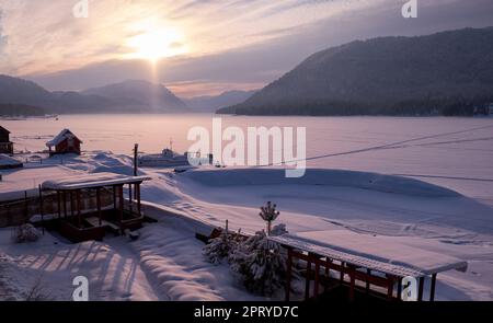 Beautiful sunset over the mountain lake Teletskoye in Altai in winter season. Stock Photo