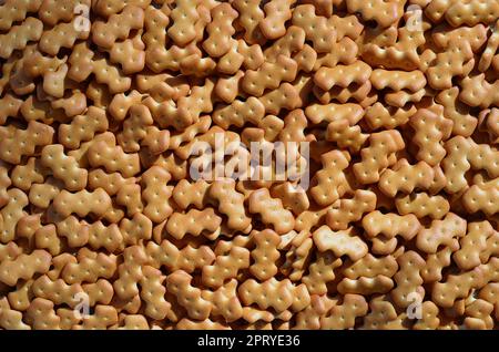 A huge bunch of salted biscuits of small sizes as a closed pattern or texture. A large amount of salted cracker in golden yellow tones Stock Photo