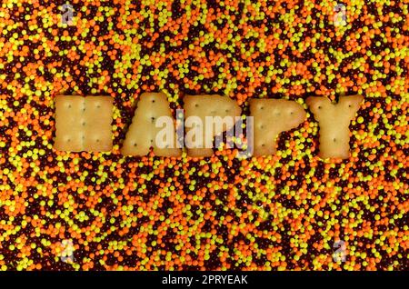 Happy. The word from the edible cracker letters lies on the glazed powder. A huge number of sweet, colorful beads of very small size for decoration of Stock Photo