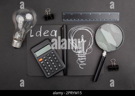 top view idea written on black notebook light bulb binder clips lupa ruler calculator on dark background Stock Photo