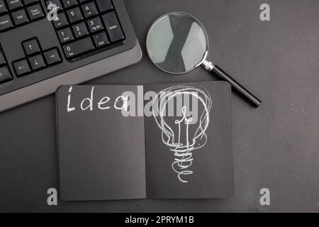 top view idea written on black notepad keyboard lupa on dark background Stock Photo