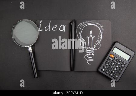top view idea written on black notebook lupa calculator pen on dark background Stock Photo