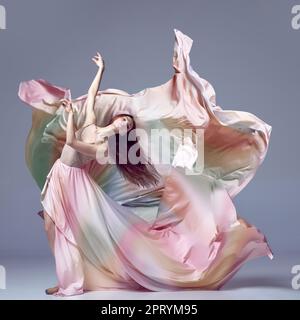 Inspired young, beautiful ballerina wearing rainbow dress dancing over grey studio background. Ballet with silk dress Stock Photo