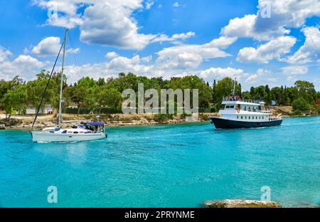 Yacht and a pleasure boat sail on the Corinth Canal in turquoise water. Scenic landscape of the Corinth Canal in a bright sunny day against a blue sky Stock Photo