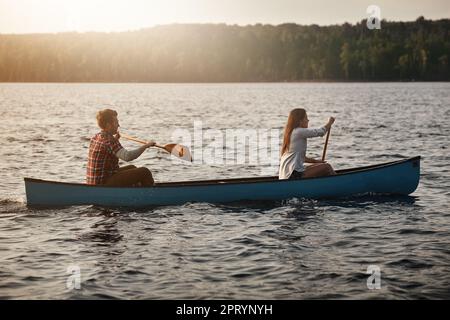 Just living life one row at a time. a young couple rowing a boat out on the lake. Stock Photo