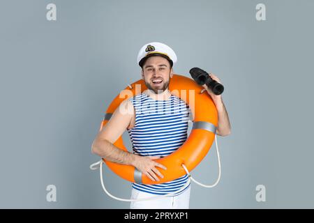 Happy sailor with binoculars and ring buoy on light grey background Stock Photo