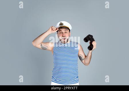 Emotional sailor with binoculars on light grey background Stock Photo