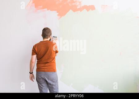 Young man using spatula and plastering of wall with white fresh finishing putty. Closeup. Repair work of home. Empty place for text. Side view Stock Photo