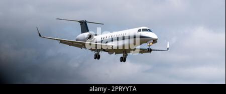 Small jet airplane with wheels down coming in for a landing with a cloudy sky in the background. Stock Photo