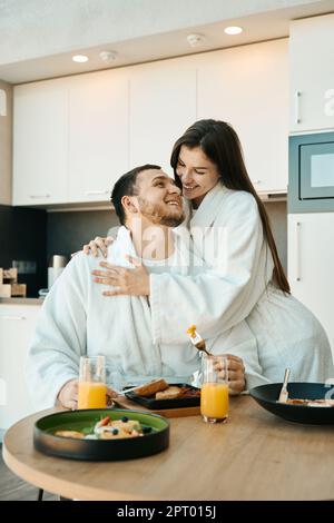 Happy young couple in bathrobes having breakfast in cozy modern kitchen Stock Photo