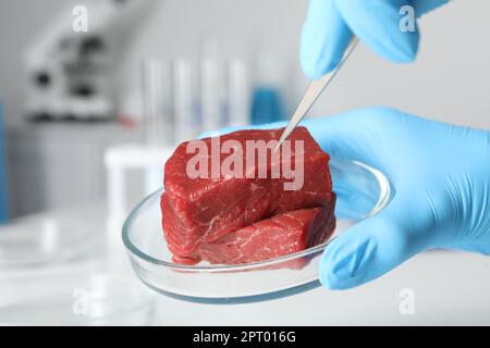 Scientist with tweezers examining piece of raw cultured meat in laboratory, closeup Stock Photo