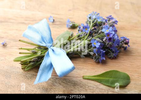 Beautiful blue forget-me-not flowers tied with ribbon on wooden table, closeup Stock Photo