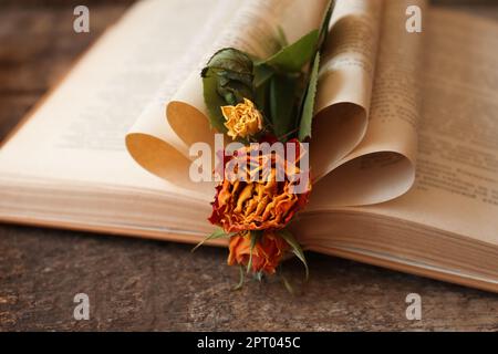 Open book with folded pages and beautiful dried flowers on wooden table, closeup Stock Photo