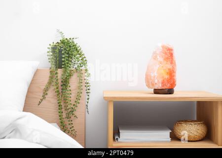 Himalayan salt lamp on wooden nightstand in bedroom Stock Photo