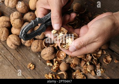 Man cracking walnuts at wooden table, closeup Stock Photo