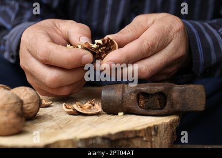 Man cracking walnuts with hammer at table, closeup Stock Photo