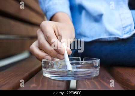 Woman putting out cigarette in ashtray on wooden bench, closeup Stock Photo