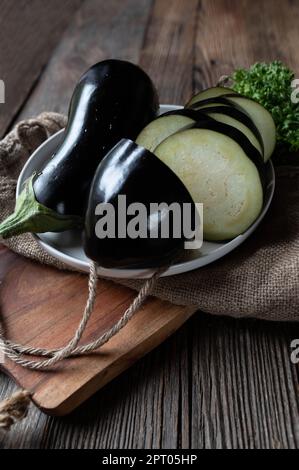Fresh, raw and uncooked whole and sliced eggplants on wooden table background. Closeup with copy space Stock Photo