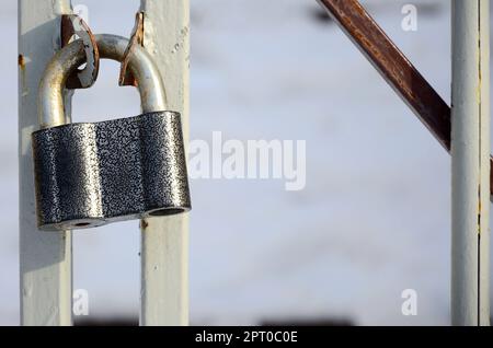 A large gray padlock hangs on a metal gate Stock Photo