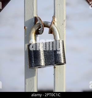 A large gray padlock hangs on a metal gate Stock Photo