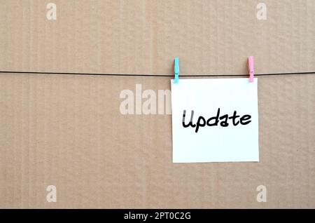 Update. Note is written on a white sticker that hangs with a clothespin on a rope on a background of brown cardboard Stock Photo