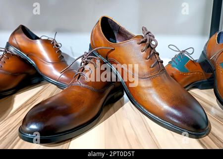 Handcrafted brown leather men shoes on the display shelves in the shoe shop. Stock Photo