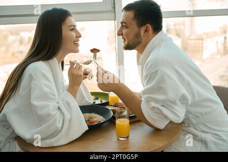 Charming young couple having a romantic breakfast in a cozy atmosphere, guys in comfortable bathrobes Stock Photo