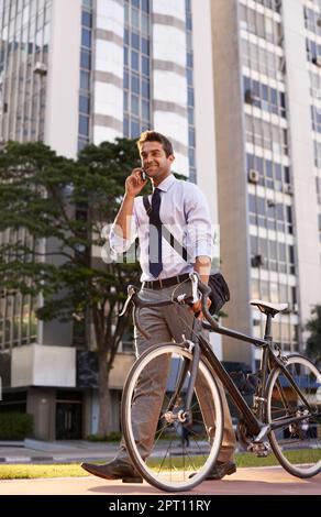 Ill be at the office in 10. a businessman taking a phone call while commuting to work with his bicycle Stock Photo