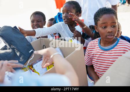 Theyre all excited to get their new school uniforms. volunteer workers handing out clothing to underprivileged children Stock Photo