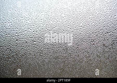 A photo of the glass surface of the window, covered with a multitude of droplets of various sizes. Background texture of a dense layer of condensate o Stock Photo