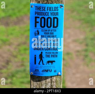 A sign on a wooden post saying 'these fields produce food - please control your dog' and 'clean up after your dog' 'bag it and bin it', England, UK Stock Photo