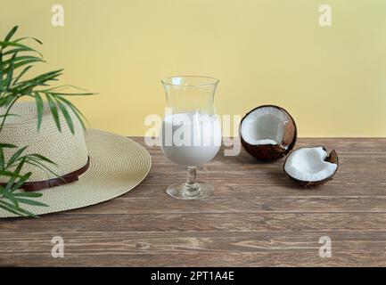 A glass of coconut milk cocktail, coconut pieces and a summer hat on wooden table Stock Photo