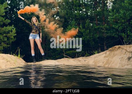 Lost hiker wagging color smoke flare to signal for help on outer wood standing by the lake Stock Photo