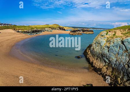 A picturesque view of the Llanddwyn Island beach in Newborough, Anglesey. Volcanic rocks and plants line the shore with a stunning sea-sky backdrop. Stock Photo