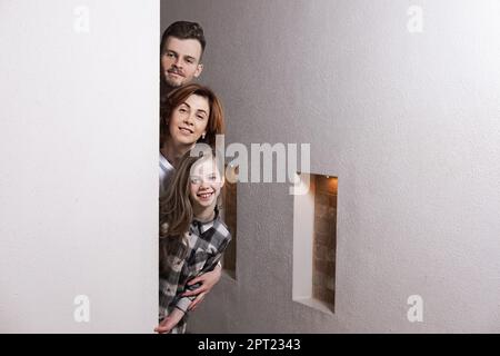 Tricky family peeks around the corner of the wall at home Stock Photo