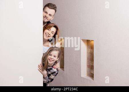 Tricky family peeks around the corner of the wall at home Stock Photo