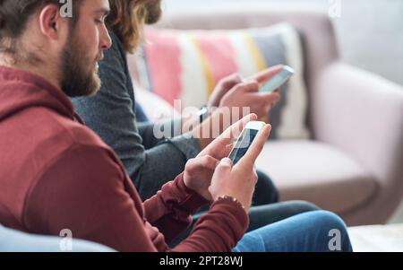Young man using smartphone browsing social media texting messages sitting on sofa with friend. Stock Photo