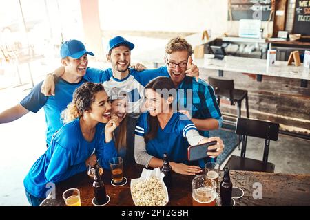 Game day fun with some our favorites. a group of friends taking a selfie while watching a sports game at a bar. Stock Photo